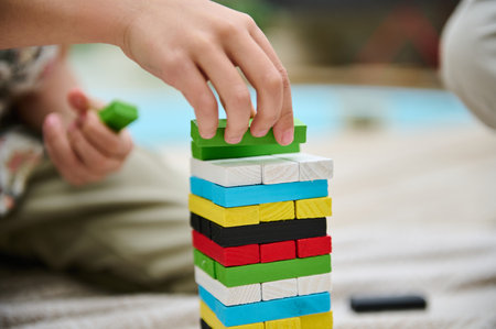 A child carefully places a green block on a vibrant stack of wooden blocks, illustrating...