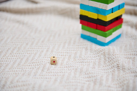 A vibrant block tower game set on a cozy patterned blanket with a wooden dice in focus. The image...