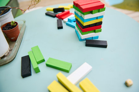 A vibrant tower of multicolored wooden blocks is stacked on a light blue table. The playful scene is complemented by scattered blocks and potted plants, suggesting a relaxed, creative atmosphere.の写真素材