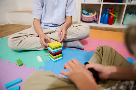 Two children engage in imaginative play, stacking colorful blocks on a foam mat. The playroom...