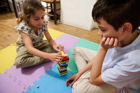 Two children are engaged in a fun and educational game, stacking colorful blocks on a bright foam mat. The setting is a cozy indoor space, encouraging creativity and concentration.の写真素材