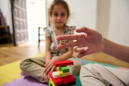 A young girl focuses intently while playing a stacking game with colorful wooden blocks. The image captures the concentration and the delicate balance required in this engaging and fun activity.の写真素材