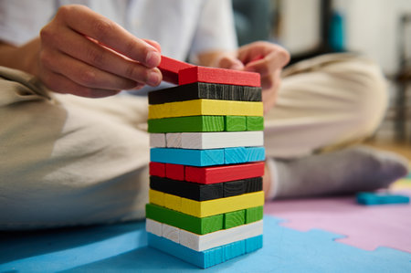 A close-up image showcases a person stacking colorful blocks on a foam puzzle mat. The focus is on the hands and vibrant wooden pieces, highlighting concentration and creativity in play.の写真素材