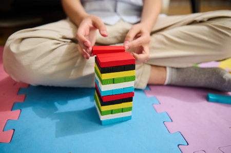 A child is engaged in playing with brightly colored building blocks placed on a soft foam play mat. The scene captures creativity, focus, and play in a warm, home environment with natural light.の写真素材
