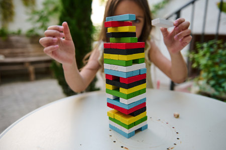 A young girl focuses intently on stacking vibrant wooden blocks into a tall tower. The outdoor setting adds to the relaxed and playful atmosphere, highlighting concentration and fun in playtime.の写真素材