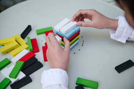 A child hands skillfully arranging a stack of colorful building blocks on a white table. The image...