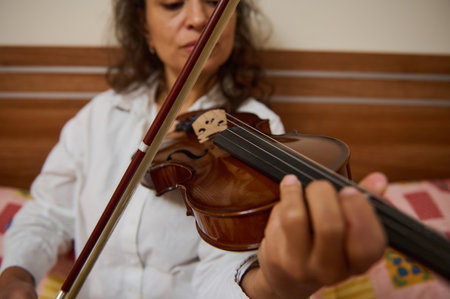 A woman skillfully plays the violin in a cozy indoor setting. Her focus and technique highlight the beauty and complexity of string music, creating an intimate musical experience.の写真素材