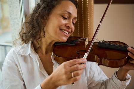 A woman with a joyful expression passionately plays the violin by a bright window. Her embrace of...