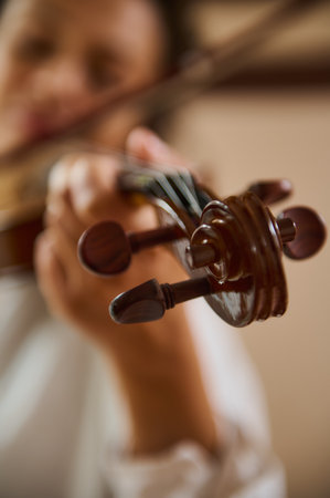 A focused view of a musician's hand adjusting the tuning pegs of a violin. The soft background highlights the intricate details of the instrument and evokes a sense of passion and artistry.の写真素材