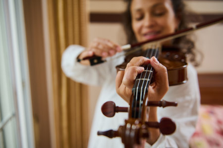 An intimate close-up image of a woman playing the violin, emphasizing her fingers skillfully manipulating the strings while the bow glides smoothly. Captures artistic expression and concentration.の写真素材