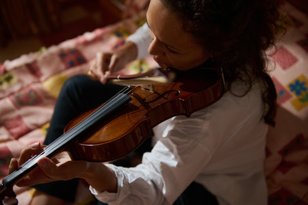 A woman passionately plays the violin while seated on a colorful quilt. The intimate home setting adds warmth to the musical moment.の写真素材