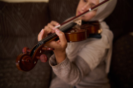 A detailed view of a woman playing the violin, capturing her focus and precision. The image highlights the intricate movements on the strings, set in a cozy home environment.の写真素材