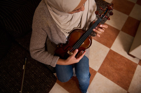 A woman in casual clothing plays the violin, focusing on practice in a cozy room.の写真素材