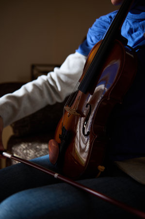 A close-up of a person playing a violin indoors, capturing the instrument and bow.の写真素材