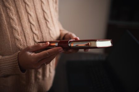 Close-up of hands holding a notebook with a pen, wearing a cozy sweater, in a warm setting.の写真素材