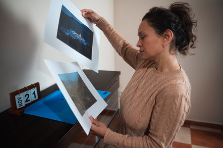 A woman reviews two landscape photographs while standing beside a desk. A calendar shows the date November 21, adding context to the scene.の写真素材