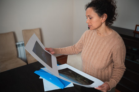 A woman examines two art prints in a warm, cozy indoor environment, appreciating the details.の写真素材