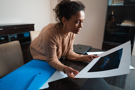 A woman in a beige sweater carefully examines a piece of artwork in a modern, comfortable home...