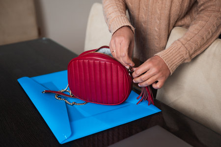 Close-up of a person fastening a strap on a chic red handbag placed on a blue folder.の写真素材