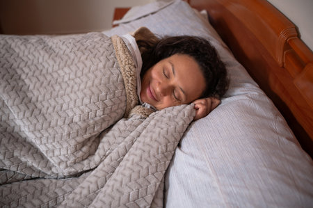 A serene woman peacefully sleeping, wrapped in a warm grey blanket on a comfortable bed, enjoying relaxation.の写真素材