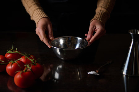 Hands hold a stainless steel bowl next to ripe tomatoes, depicting a cooking scene. The dark background highlights the vibrant red tomatoes and kitchenware, capturing the essence of culinary preparation.の写真素材