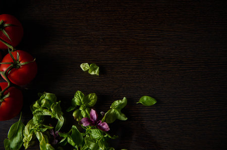 Ripe red tomatoes accompanied by fresh basil leaves are displayed against a dark wooden background, creating a rustic, natural vibe ideal for culinary themes and healthy lifestyle concepts.の写真素材