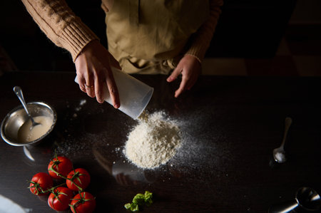 Hands preparing to cook with flour and fresh tomatoes on a dark kitchen counter.