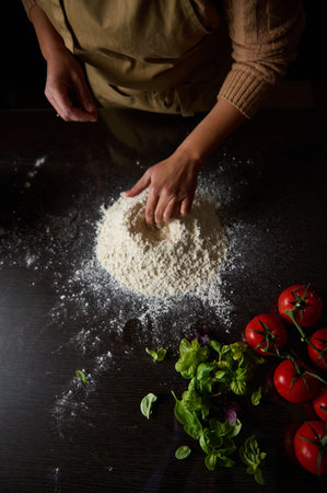 A cook's hand mixes flour amidst fresh tomatoes and herbs, showcasing culinary preparation in a rustic setting.の写真素材
