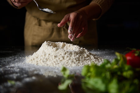 Close-up of hands preparing dough with flour and salt, showcasing fresh ingredients in a cozy kitchen atmosphere.の写真素材