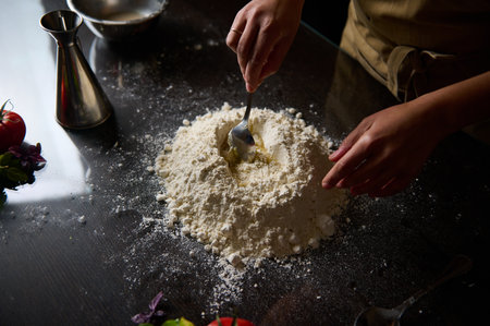 A chef expertly prepares fresh pasta dough by hand, mixing flour and eggs on a dark surface.