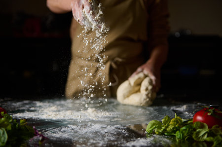 A chef tosses flour onto a surface while kneading dough, surrounded by fresh herbs and tomatoes, in...
