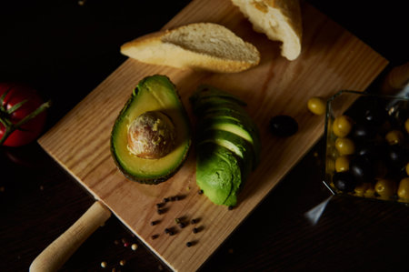 A rustic presentation of fresh sliced avocado with bread and assorted olives on a wooden board.