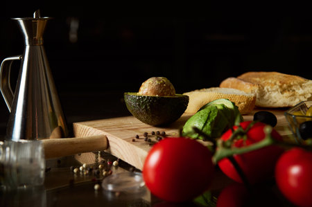 A wooden board displays fresh ingredients for guacamole and bruschetta, including avocado, tomato, and bread, set beside an oil canister and spices, suggesting a rustic culinary experience.の写真素材