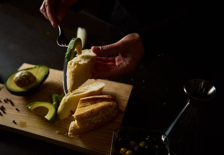 Close-up of hands preparing a fresh avocado and bread snack on a cutting board, emphasizing...