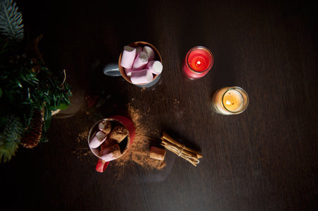 A cozy winter scene featuring hot cocoa topped with marshmallows, surrounded by burning candles and...