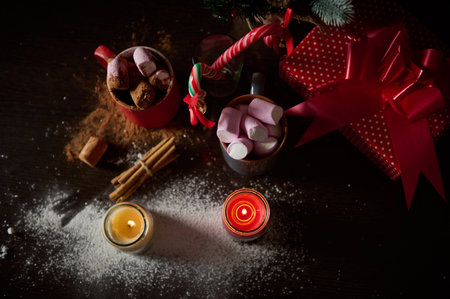 Cozy holiday scene featuring mugs of hot chocolate, marshmallows, cinnamon, candles, and a wrapped gift. Bright and festive decor ideal for celebrating Christmas or the winter season.の写真素材