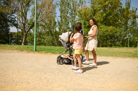 A mother with her children enjoying a sunny day at the park. They are beside a stroller under the...