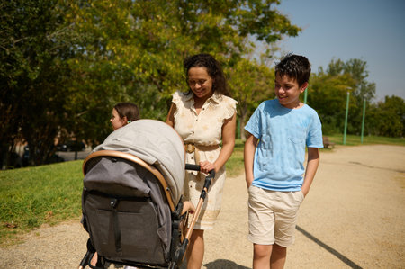 A joyful family strolls through a sunlit park, pushing a stroller. The setting exudes happiness and togetherness, capturing a serene outdoor moment.の写真素材