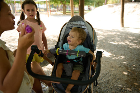 A joyful family gathering in a sunny park, featuring children and a baby in a stroller. Emphasizes childhood happiness, outdoor play, and family bonds.の写真素材