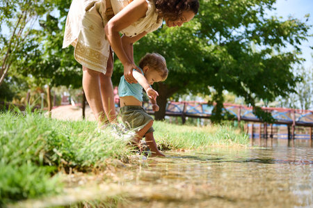 A mother and her young child enjoy a sunny moment by a tranquil lakeside, experiencing nature together and exploring the water's edge.の写真素材