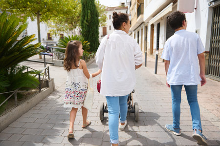 A family enjoys a leisurely walk on a sunny day, exploring a charming street lined with greenery.の写真素材