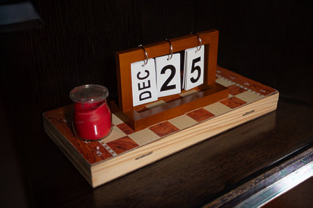 A desktop decoration featuring a wooden calendar marking December 25, accompanied by a red candle on...