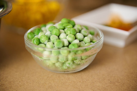A close-up of a glass bowl filled with frozen green peas on a table. Ideal for use in food, health, and cooking-related projects, illustrating freshness and storage.の写真素材