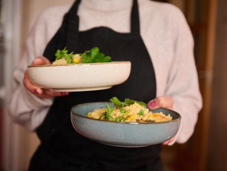 Close-up of a person holding two bowls filled with rice and vegetables, garnished with herbs. The bright and nutritious dish emphasizes healthy eating and culinary presentation.の写真素材