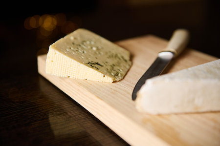 A selection of gourmet cheeses on a wooden board, accompanied by a knife. Ideal for culinary presentations or food photography, emphasizing elegant and delicious dining experiences.の写真素材
