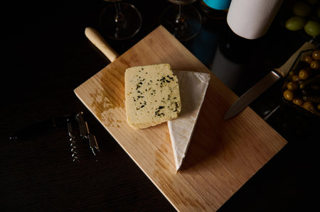 Delicious gourmet cheeses displayed on a wooden board with glasses of wine and appetizers.の写真素材