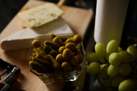 A gourmet cheese board with pickles, green grapes, and soft cheeses, artistically presented. Ideal for culinary and hospitality themes, showcasing a stylish and delectable arrangement.の写真素材