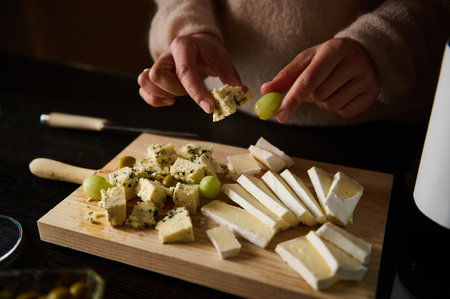 A cozy atmosphere, showcasing hands preparing a cheese platter with grapes on a wooden board.の写真素材