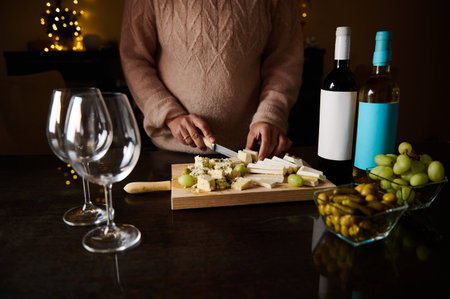 A cozy setup of hands arranging cheese, wine bottles, and glasses on a festive evening.の写真素材