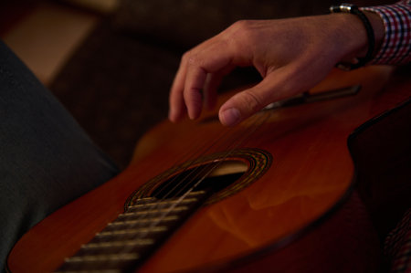 A detailed close-up view of fingers gently strumming the strings of a wooden acoustic guitar. The...